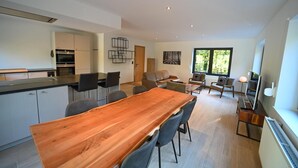 Une cuisine moderne dotée d’appareils électroménagers intégrés, un coin repas avec une table et des chaises en bois, et un espace salon avec un canapé et des fauteuils.