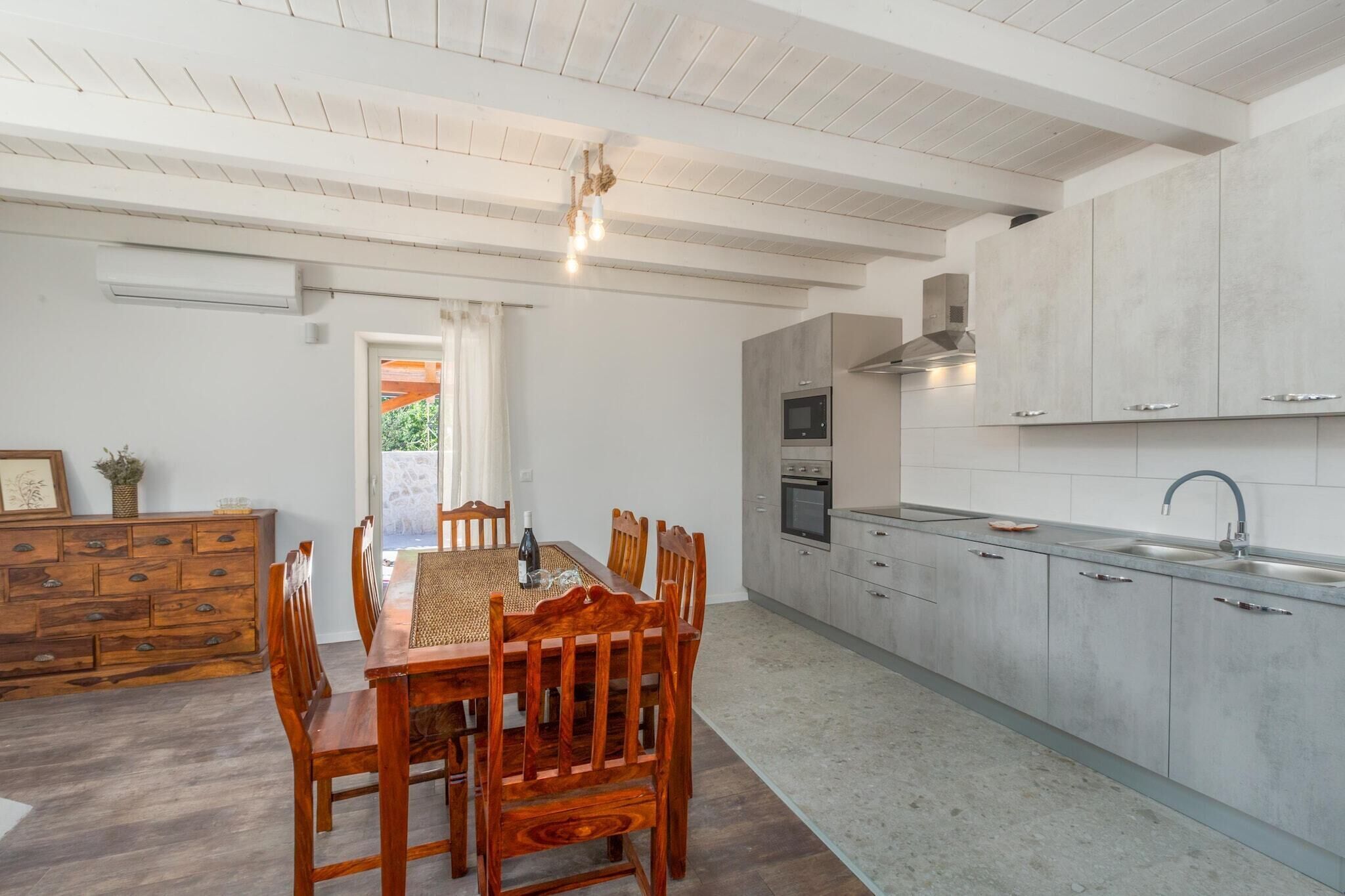 A modern kitchen with white cabinets, a dining area with a wooden table and chairs, and a built-in oven.