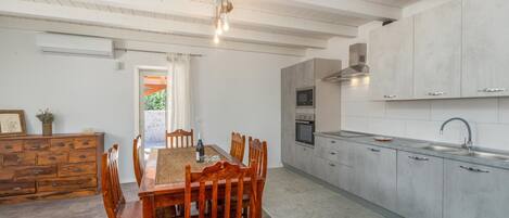 A modern kitchen with white cabinets, a dining area with a wooden table and chairs, and a built-in oven.