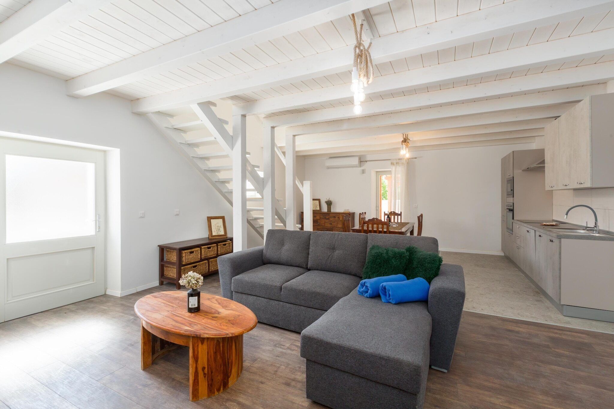 A spacious living area with a gray sectional sofa, a wooden coffee table, and a kitchen in the background.