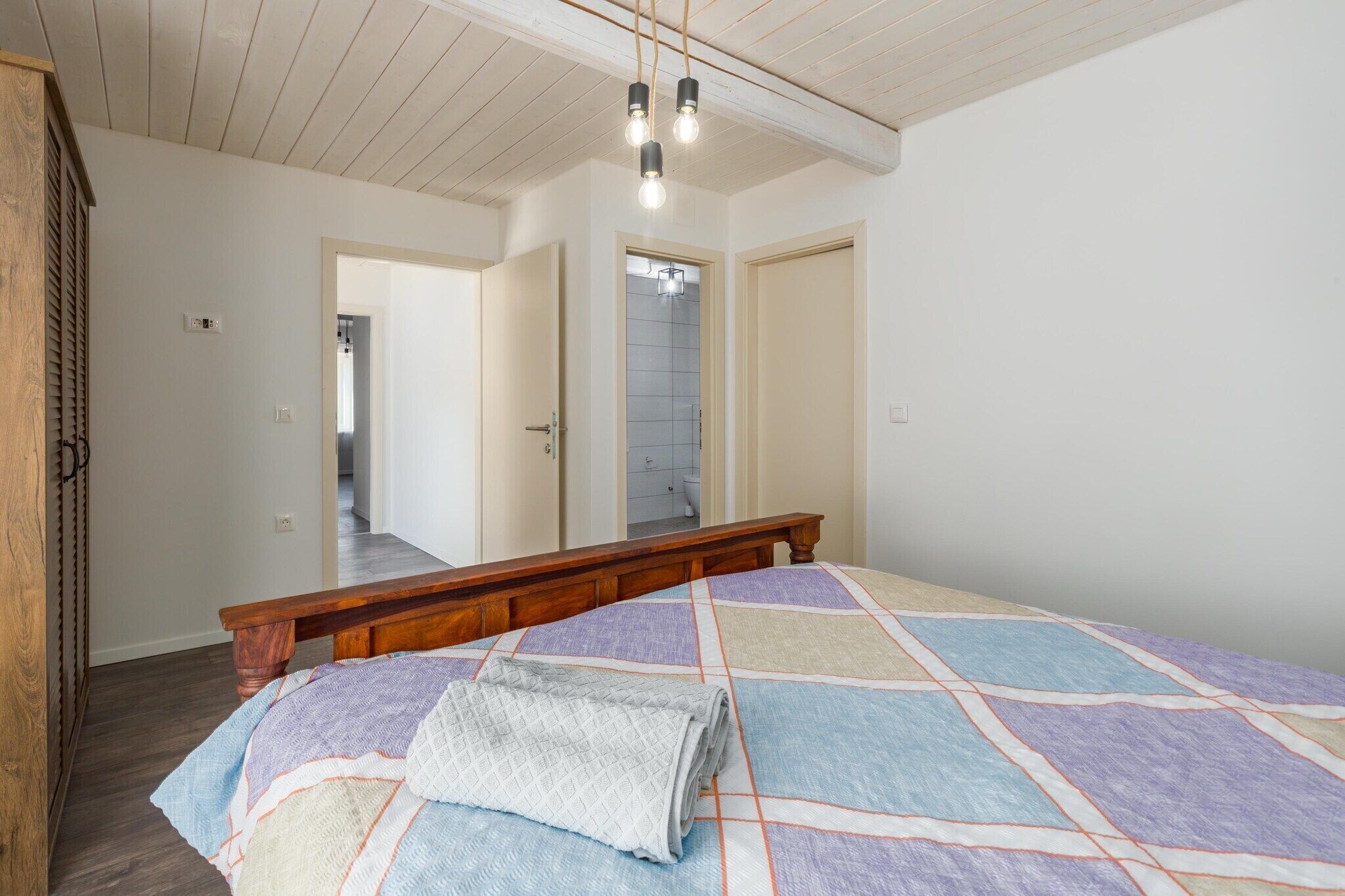 A bedroom with a wooden bed frame, a quilted bedspread, and a hanging light fixture.