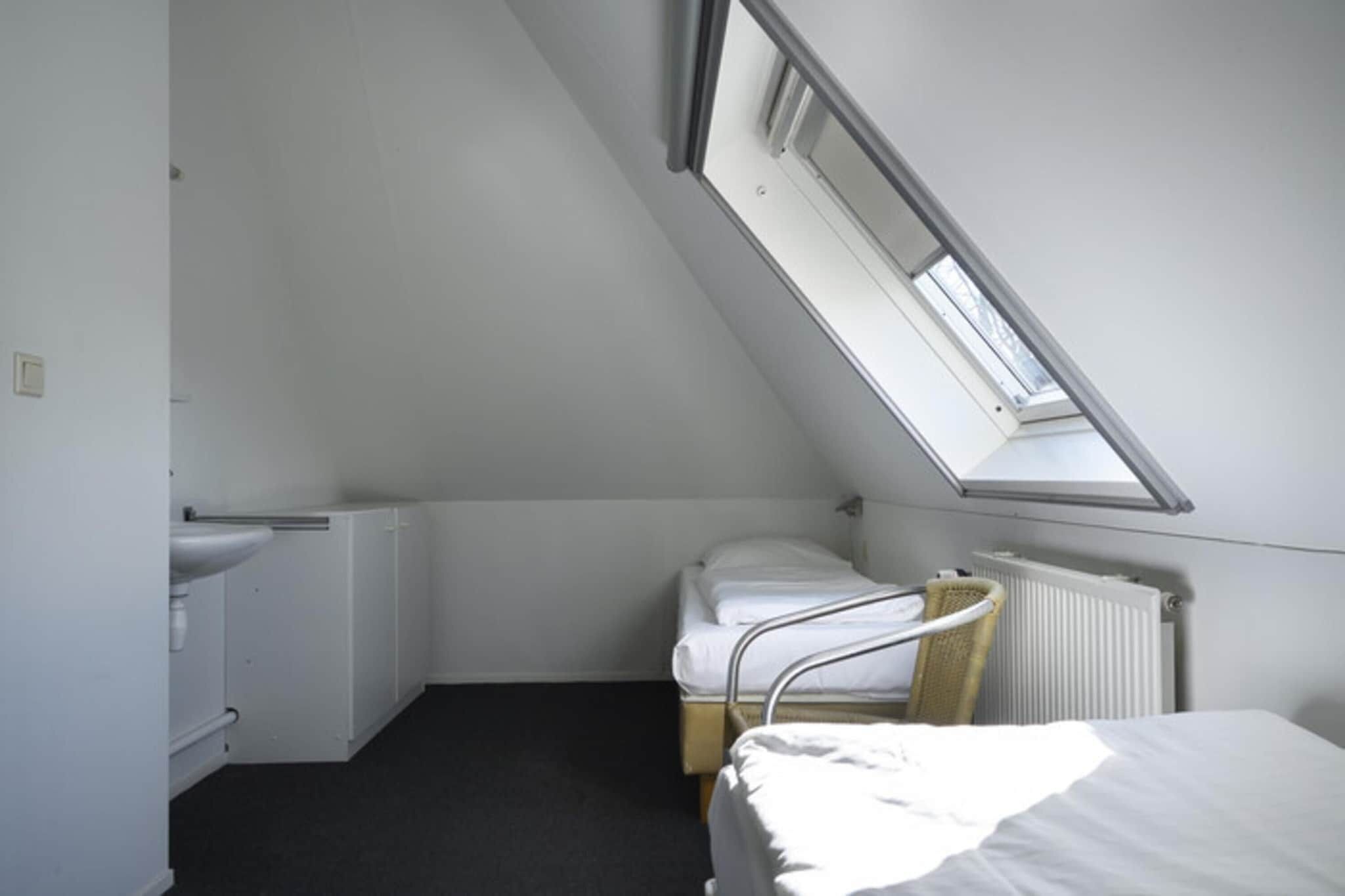 A small, simple room with a sloped ceiling, a bed, a radiator, and a skylight.