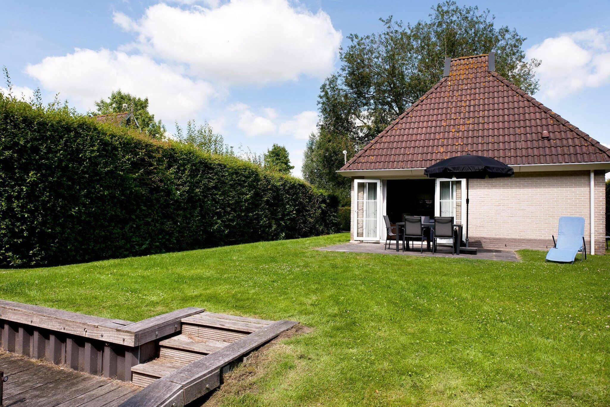 A small brick house with a tiled roof, a patio with outdoor furniture, and a wooden deck.