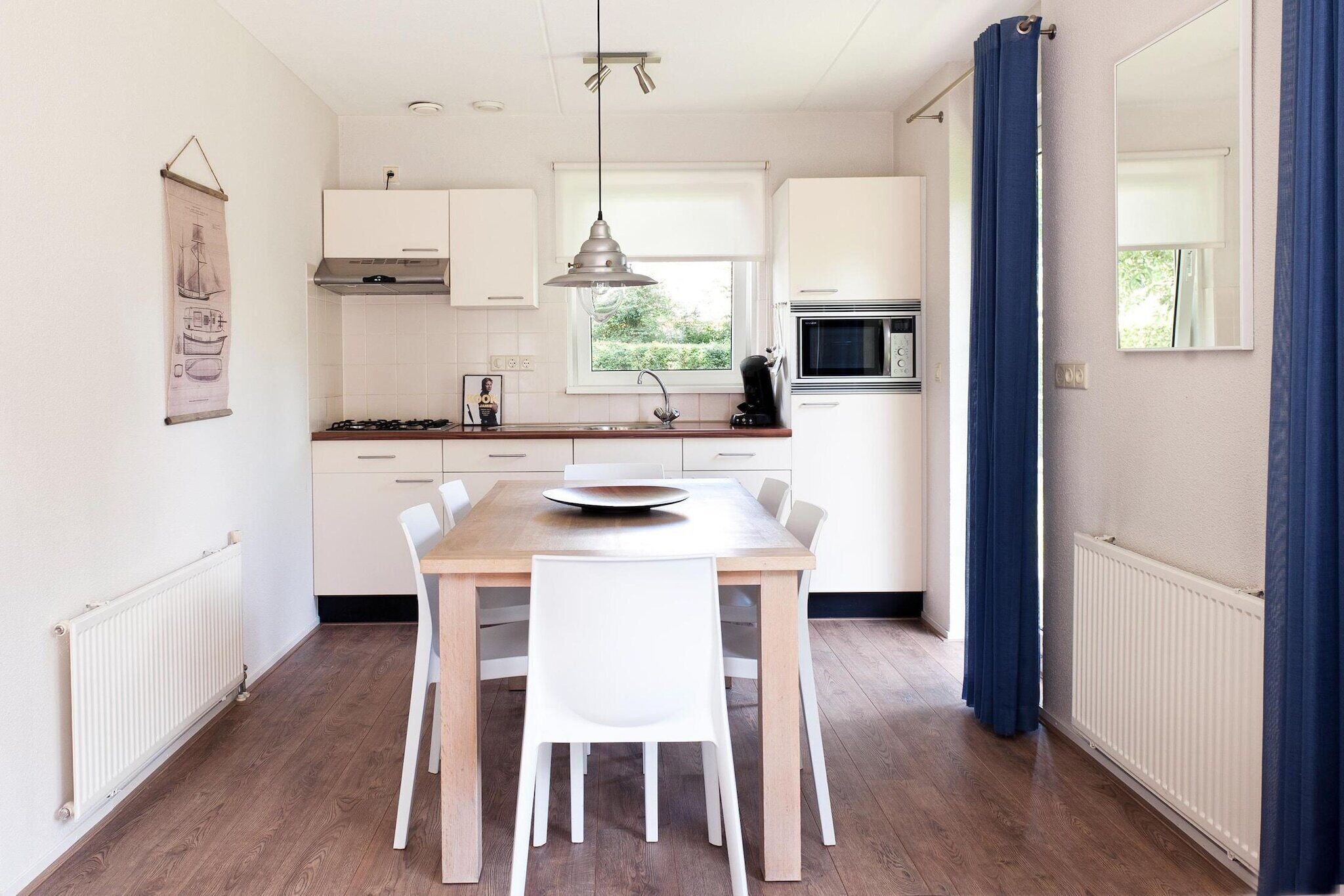 A modern kitchen with white cabinets, a wooden dining table, and a hanging pendant light.