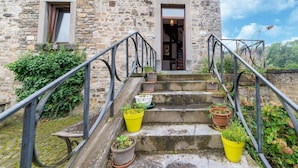 A stone building with a staircase leading to a door, surrounded by potted plants and a metal railing.