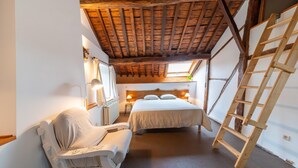 A bedroom with a wooden ceiling, a bed, a chair, a ladder, and a window.