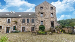A stone building with a courtyard, featuring a central staircase, a bench, and potted plants.