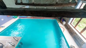An indoor swimming pool with clear water, wooden beams overhead, and a stone wall on one side.