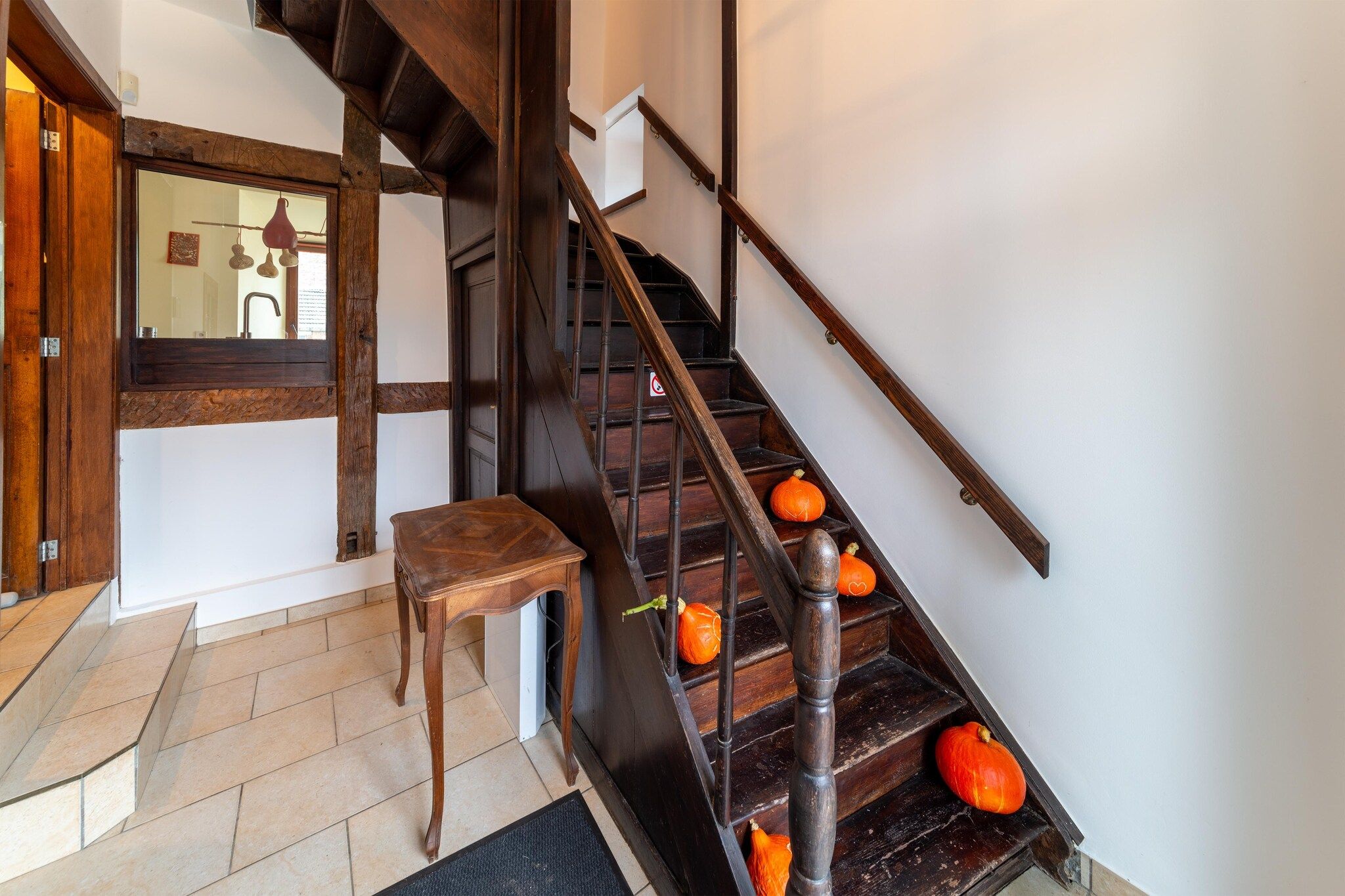 Un escalier en bois avec une rampe, une petite chaise en bois et des citrouilles disposées sur les marches.