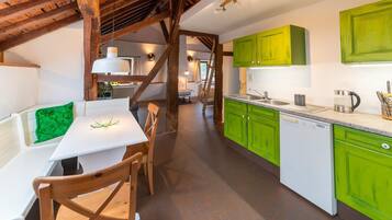 Een keuken met groene kasten, een witte vaatwasser en een houten eettafel met stoelen.