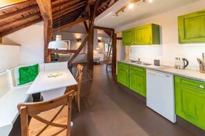 Une cuisine avec des meubles de rangement verts, un lave-vaisselle blanc et une table à manger en bois avec des chaises.