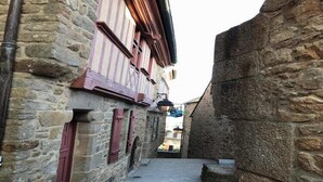 Un estrecho callejón empedrado entre edificios con contraventanas de madera y una pared de piedra a un lado.
