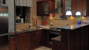 A modern kitchen with dark wooden cabinets, a stainless steel refrigerator, a built-in oven, and a large island with a sink. - Vector Home (Warsaw)