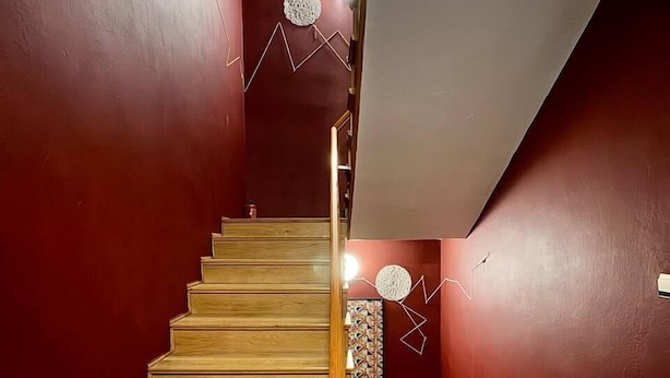A wooden staircase with a handrail leading to a landing with a red wall and geometric wall art. - Vector Home (Warsaw)
