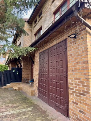 A brick building with a large garage door, a wooden porch, and a black fence. - Vector Home (Warsaw)