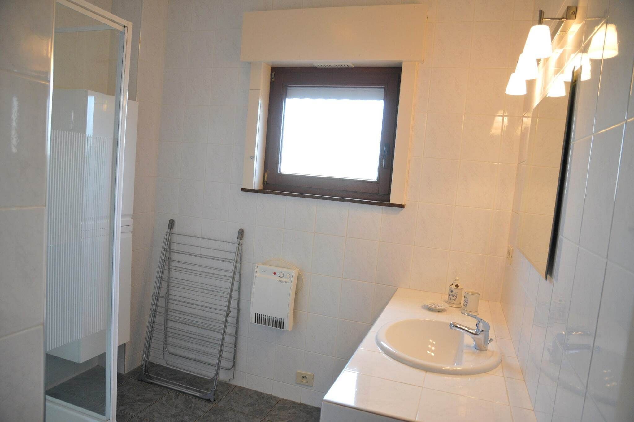 A bathroom with a window, a towel rack, a heater, and a sink.