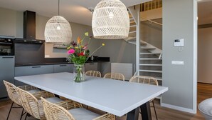 A modern kitchen with a white table and wicker chairs, a vase of flowers, and a staircase. - Stylish Marina Loft w/Balcony (Kamperland)