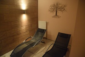 A waiting area with two black lounge chairs, a wooden wall, a wall-mounted light, and a radiator.