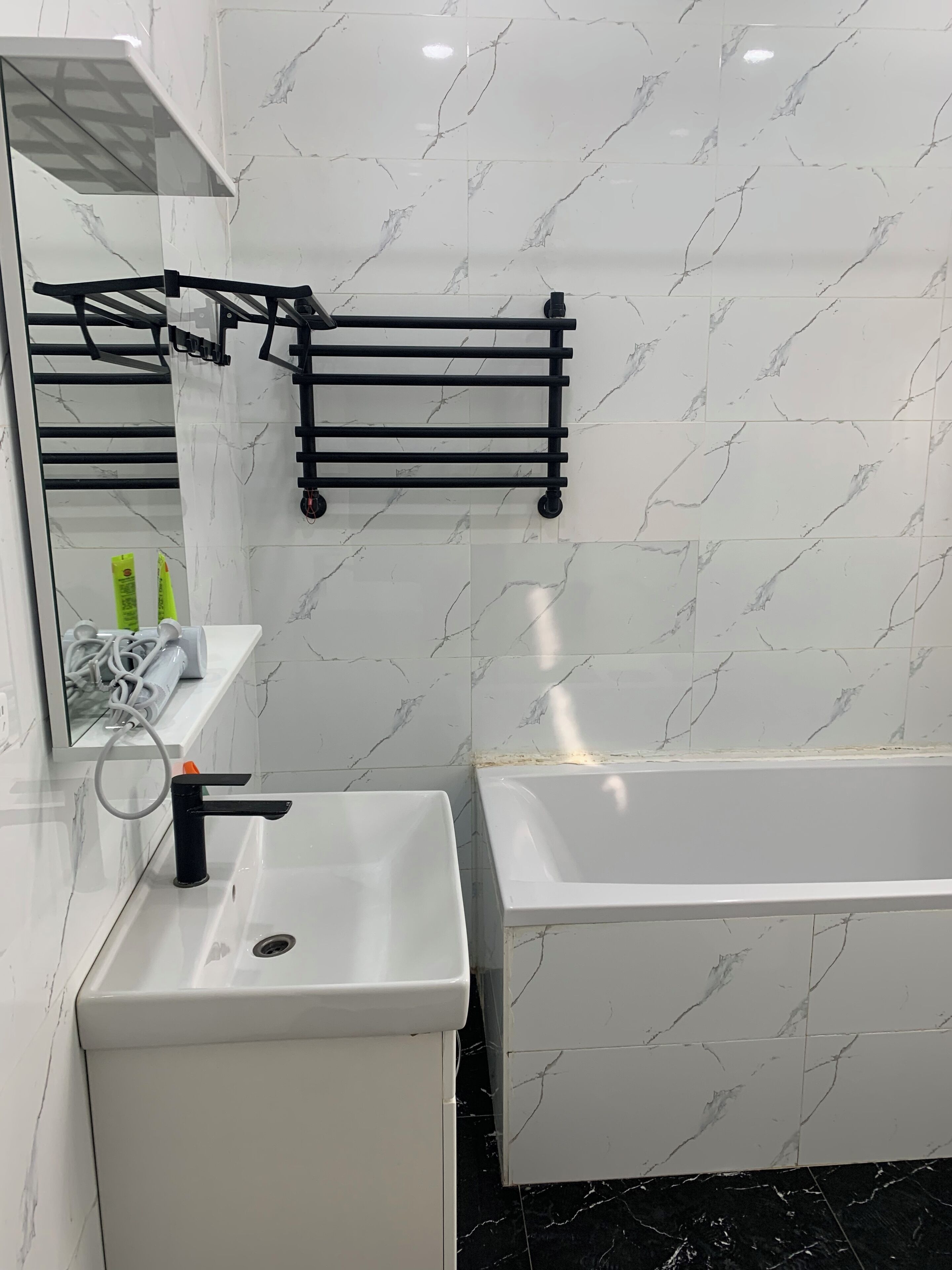 Une salle de bain moderne avec un lavabo blanc, un porte-serviettes noir, un miroir et une baignoire.