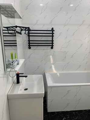 A modern bathroom with a white sink, a black towel rack, a mirror, and a bathtub. - MuTu Hotel (Almaty)