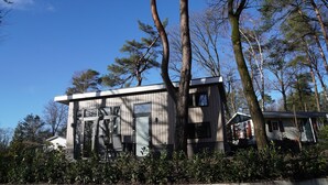 A modern house with a large glass door, surrounded by trees and a clear blue sky. - Forest-View Tiny House (Hoenderloo)