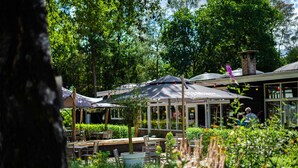 An outdoor seating area with tables and umbrellas, surrounded by lush greenery and trees. - Forest-View Tiny House (Hoenderloo)