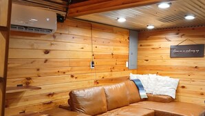 Accogliente interno di una baita con un divano in pelle marrone, pareti in legno e un cartello con su scritto: 'Avventatevi dentro e rilassatevi'.