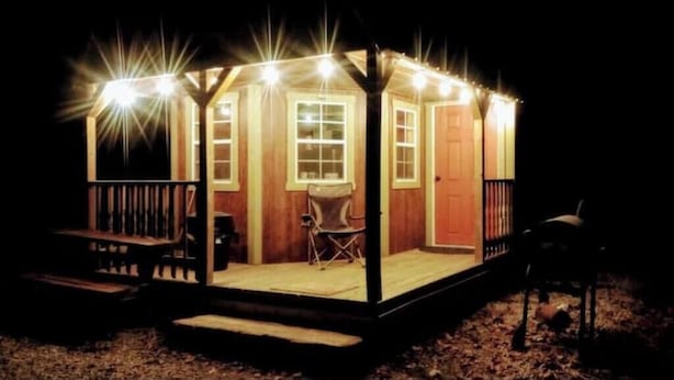 Una piccola costruzione in legno illuminata, con un portico, un tavolo e due sedie.