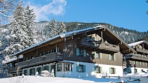 Un immeuble en bois à plusieurs étages, doté de balcons, entouré d’arbres et de montagnes couverts de neige.