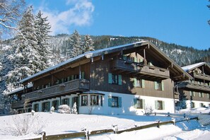 A multi-story wooden building with balconies, surrounded by snow-covered trees and mountains. - Alpenglück am Wendelstein (Bayrischzell)