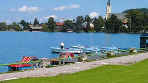 A lakeside view with boats docked along the shore, a church with a tall steeple, and residential buildings in the background. - Alpenparadies am Wendelstein (Bayrischzell)