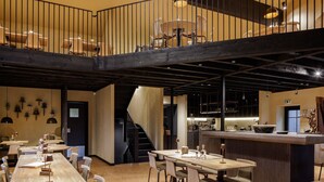 A spacious dining area with multiple tables and chairs, a central bar area, and a staircase leading to an upper level. - Cozy Luxembourg Apartment (Neufchâteau)