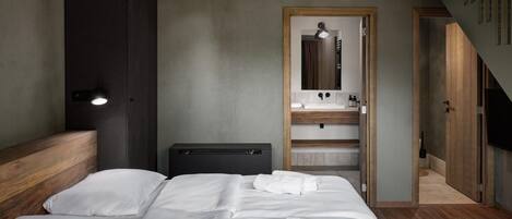 Une chambre d’hôtel moderne dotée d’un grand lit, d’une tête de lit en bois, d’une armoire intégrée, d’une coiffeuse avec un miroir et d’un petit coin salon.