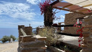 Een stenen gebouw met een pergola, uitzicht op zee en bloeiende planten.