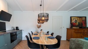 Een eetgedeelte met een houten tafel, zwarte stoelen, een moderne hanglamp en een televisie aan de linkerkant.