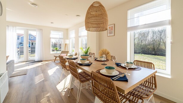 A dining area with a long table, wicker chairs, and a hanging light fixture. - Holiday home with lots of privacy (Simonshaven)