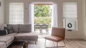 Een moderne woonkamer met een grijze modulaire bank, een ronde salontafel, een bruine leren fauteuil en een eethoek met een tafel en stoelen.