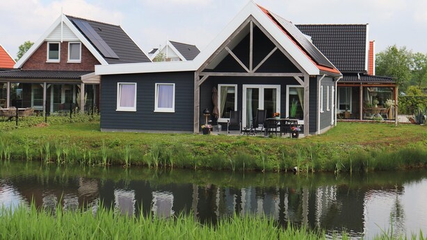 Een huis met een vijver ervoor, een overdekte veranda en een eethoek met buitenmeubilair.