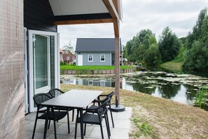 A patio with a table and chairs, a pond, and a house in the background. - Nice holiday home near the waterfront (Zuid-Holland)