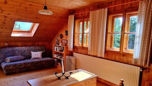 A cozy wooden cabin with a sloped ceiling, a sofa, a table with a candle, a bookshelf, and a window with curtains. - Alpine Hut in Murau near Ski Slope (St. Lorenzen ob Murau)