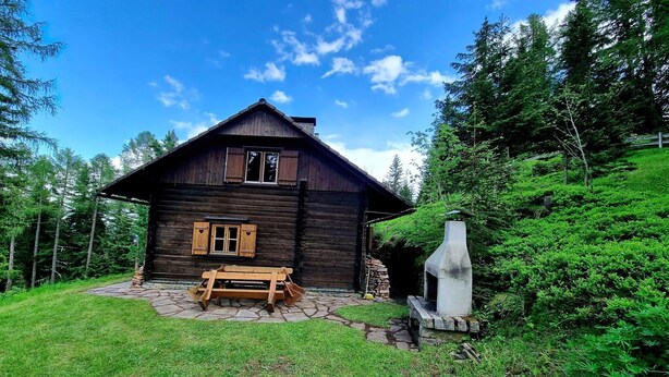 A wooden cabin with a stone patio, a bench, and a stone fireplace. - Alpine Hut in Murau near Ski Slope (St. Lorenzen ob Murau)