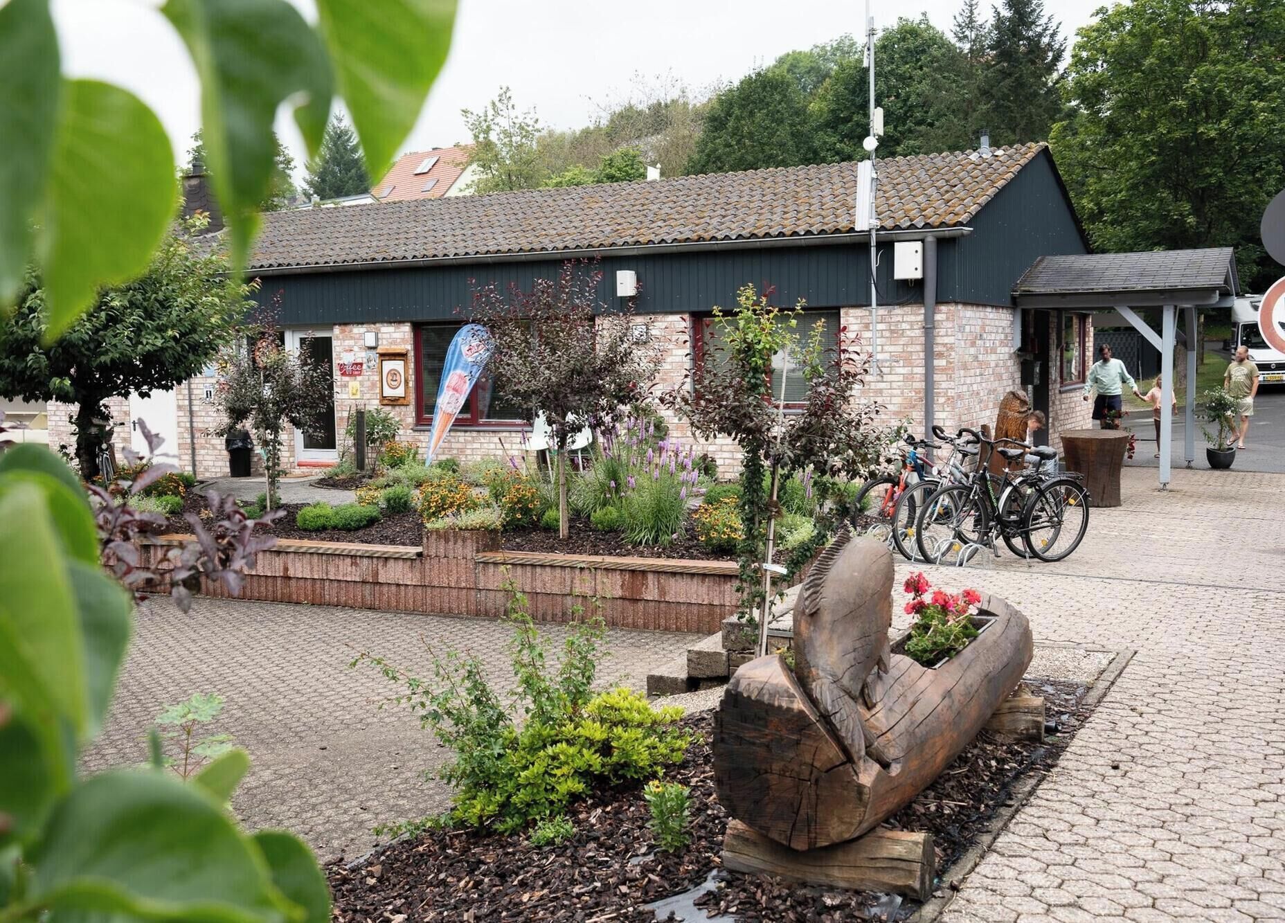 A building with a tiled roof, a brick facade, and a garden area with plants and a wooden sculpture.