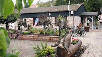 Een gebouw met een pannendak, een bakstenen gevel en een tuin met planten en een houten sculptuur.