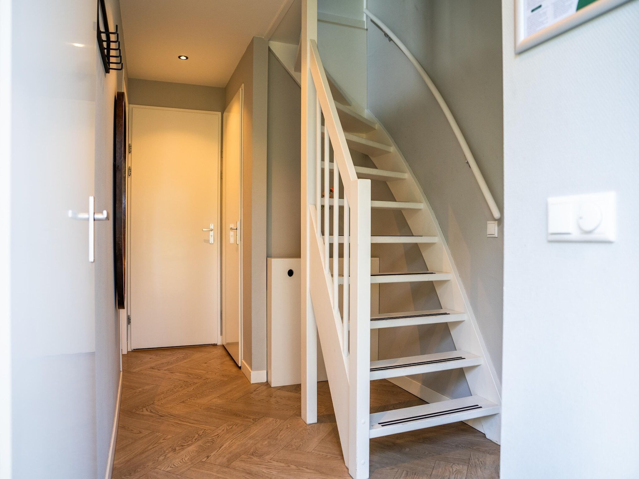 A modern interior with a wooden floor, white walls, and a white staircase.