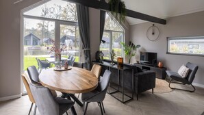 Un espace repas moderne avec une table et des chaises en bois, un téléviseur et une vue sur l’extérieur.