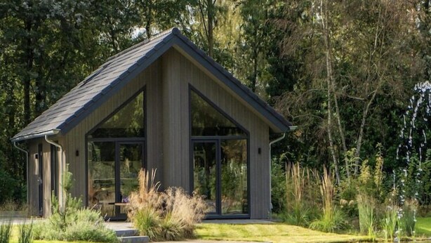 Une maison moderne avec un toit en pente, de grandes fenêtres en verre et un petit quai s’avançant dans un étang.