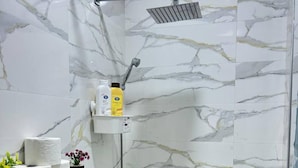 A bathroom with a shower, marble walls, a toilet paper holder, and a small shelf with toiletries. - Fontana apartamento3 (Tanger)