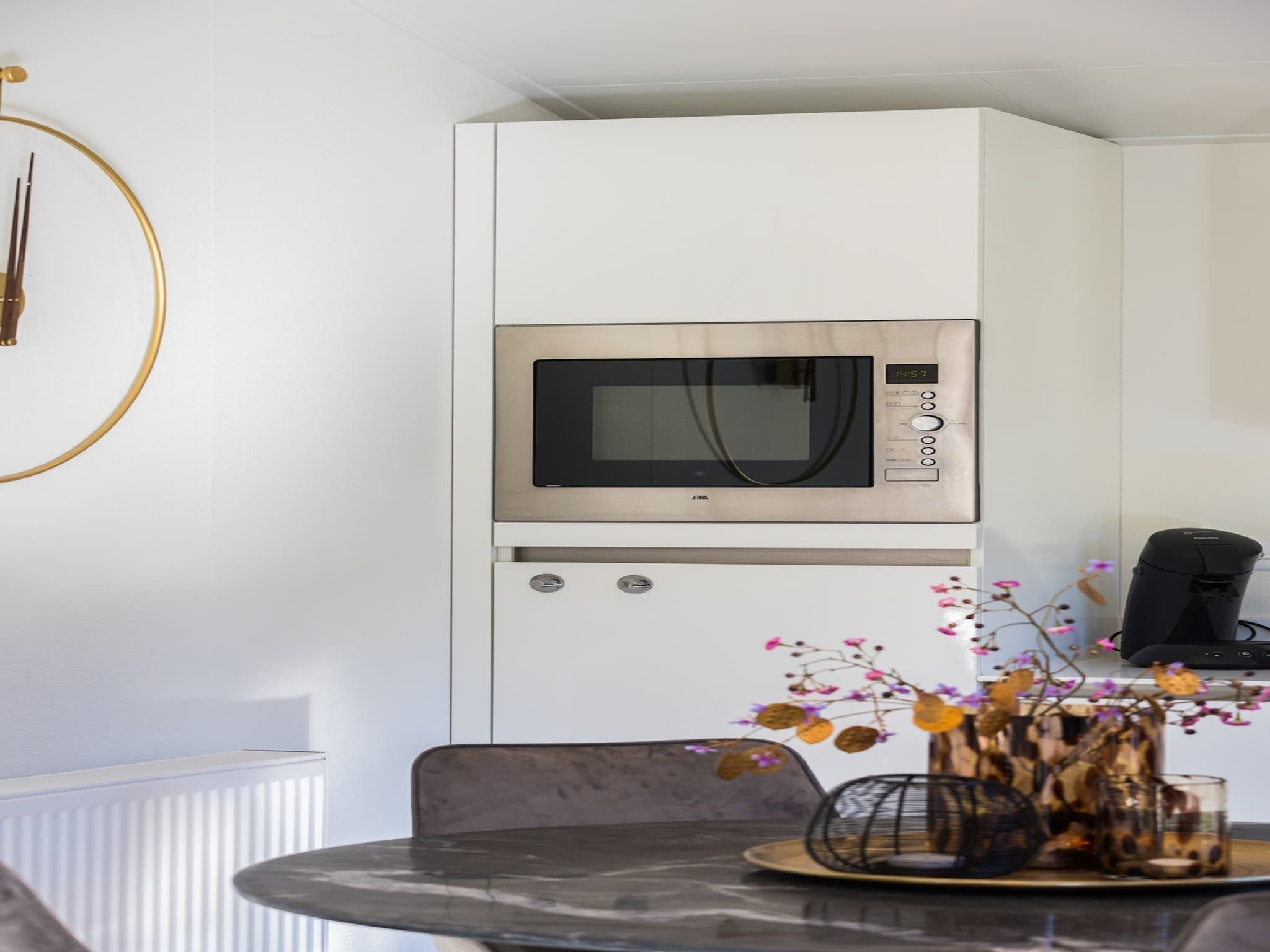 A modern kitchen with a built-in microwave, a coffee machine, and a dining area with a table and chairs.