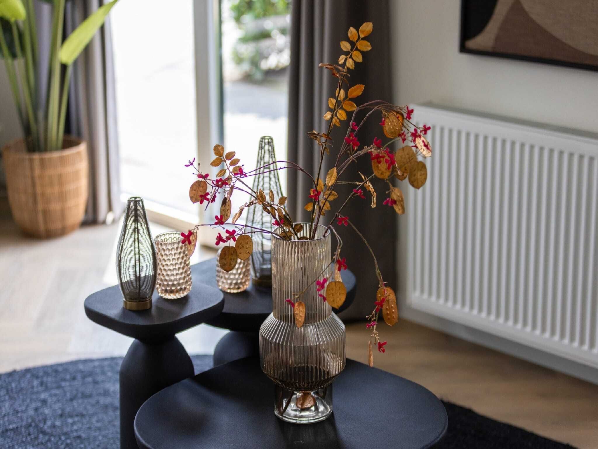 Een kamer met een modern interieur, met een zwart ronde tafel met een glazen vaas met gedroogde bloemen en bladeren, en twee glazen vazen met reliëfdecoratie.