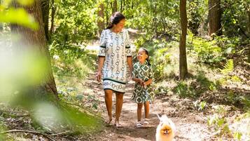 A woman and a child walking a small dog on a dirt path in a forested area.
